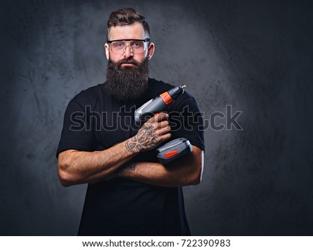 stock-photo-the-brutal-bearded-tattooed-male-holds-a-drill-over-grey-background-722390983.jpg